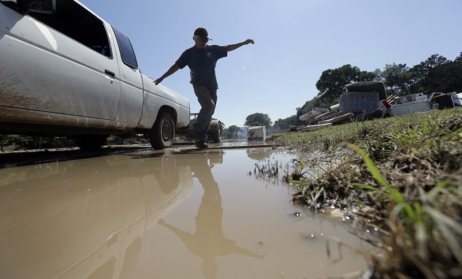 Johnny  Rodriguez uses a plank to cross standing water as he works along the Blanco River, Friday, May 29, 2015, in Wimberley, Texas. Search efforts continue for those persons who went missing from the Memorial Day weekend floods in Central Texas. (AP Photo/Eric Gay)