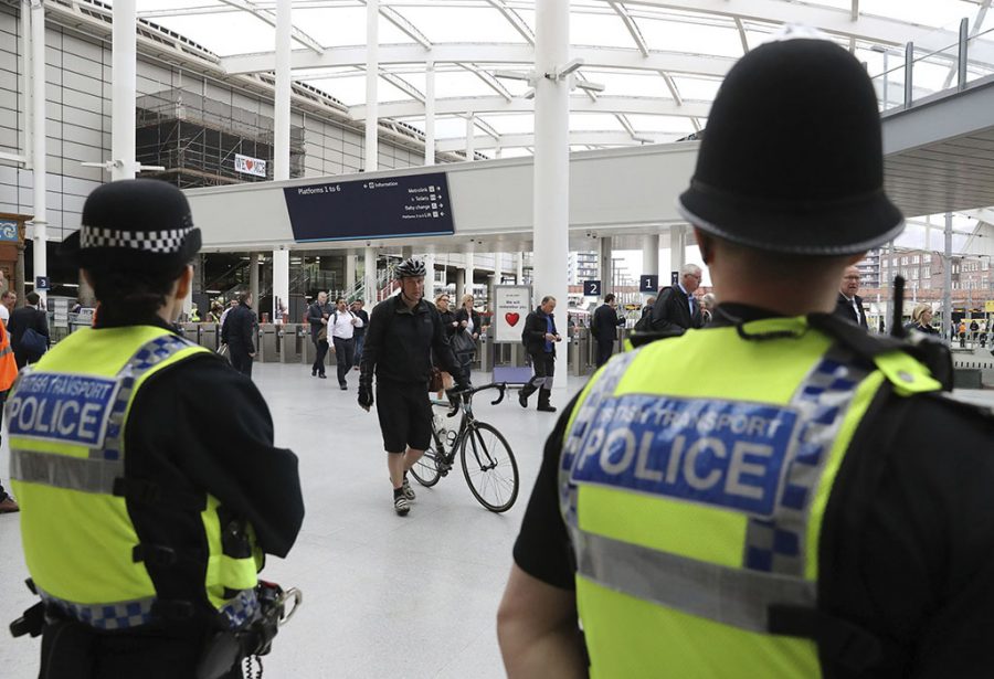 Police watch as commuters pass through Manchester Victoria railway station in Manchester England, which has reopened for the first time since the terror attack on the adjacent Manchester Arena May 30, 2017.  (Owen Humphreys/PA via AP)
