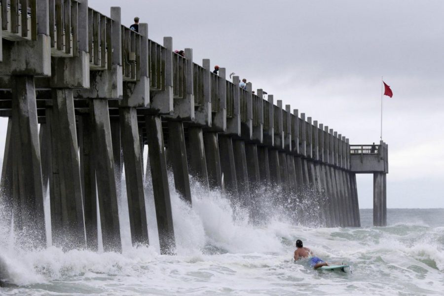 Waves crash into a pier as a surfer rides the waves.