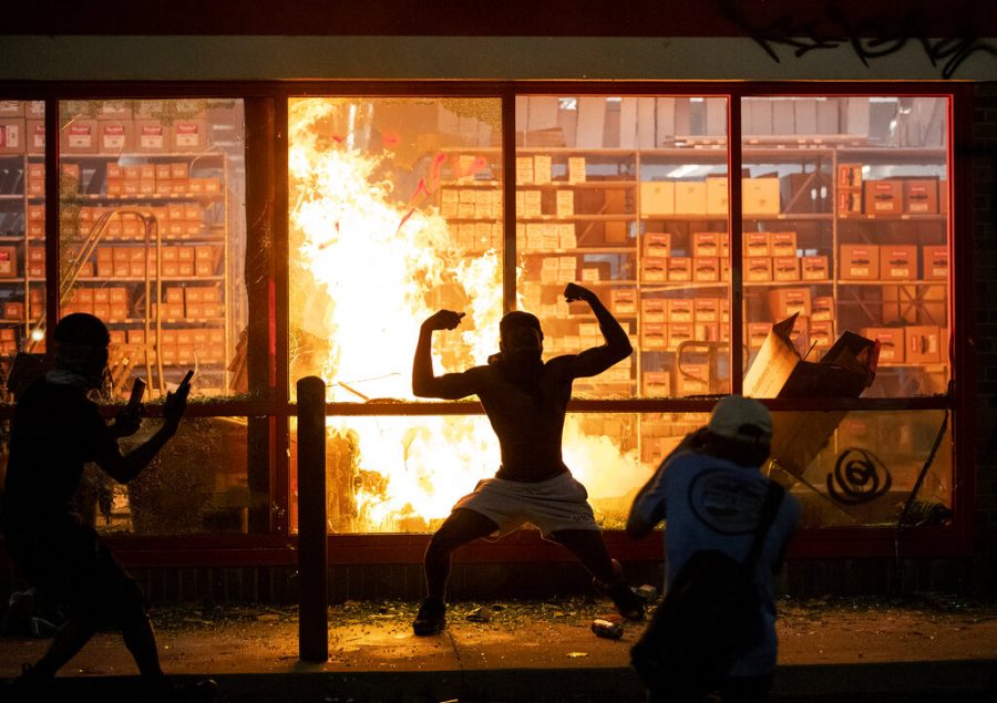 A man poses for photos in front of a fire at an AutoZone store, while protesters hold a rally for George Floyd in Minneapolis on Wednesday, May 27, 2020. Violent protests over the death of the black man in police custody broke out in Minneapolis for a second straight night Wednesday, with protesters in a standoff with officers outside a police precinct and looting of nearby stores.