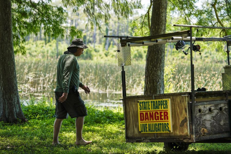 An alligator trapper walks through a wooded area near a lake. A sign reads State trapper, danger, alligators.