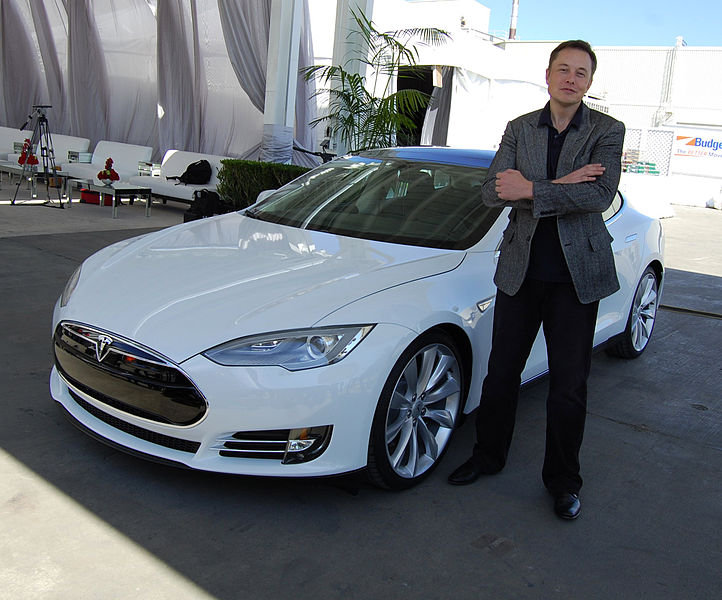 Elon Musk stands next to a Tesla.