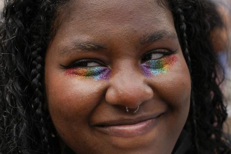 A dark-haired protester wearing rainbow eyeshadow smiles.