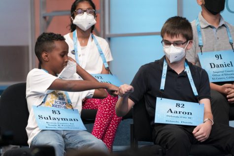 Two spelling bee contestants fist bump in the stands.