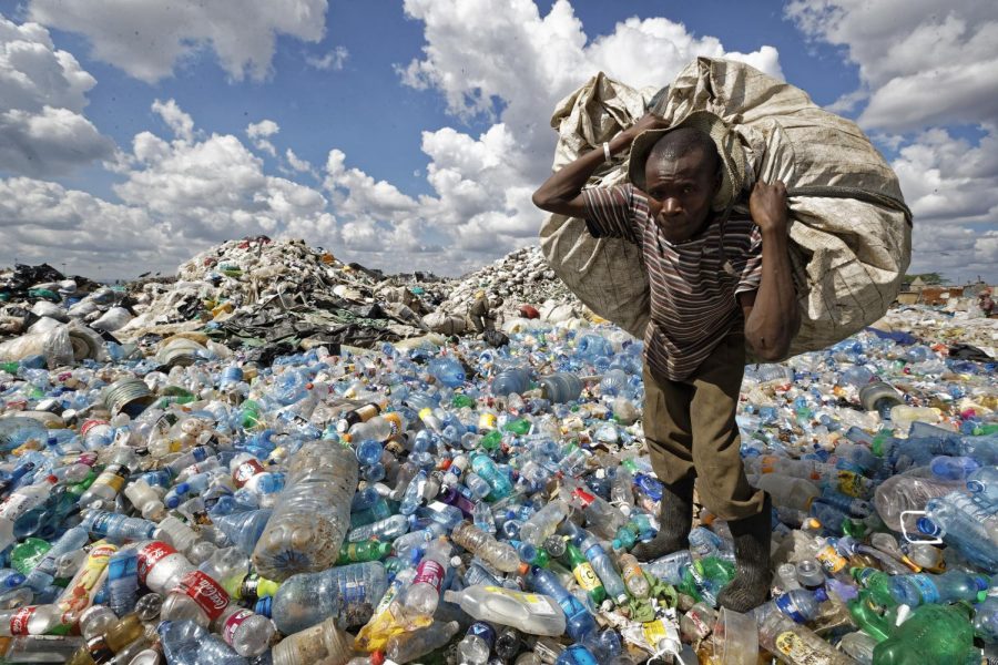 A man walks on a mountain of plastic bottles as he carries a sack of them to be sold for recycling in the Dandora slum of Nairobi, Kenya, Dec. 5, 2018. 
